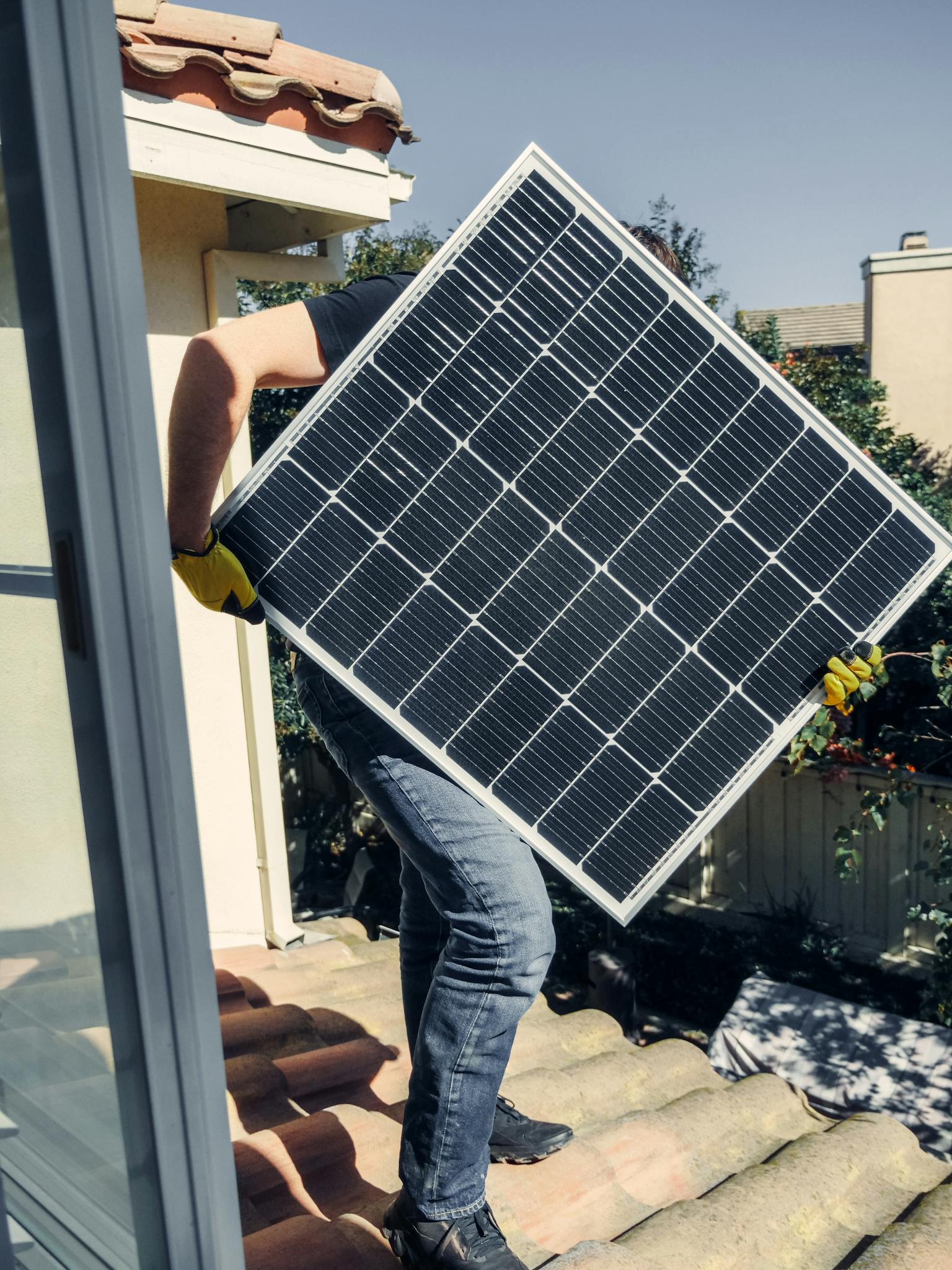 A worker carrying a solar panel for installation on a sunlit rooftop, showcasing clean energy.