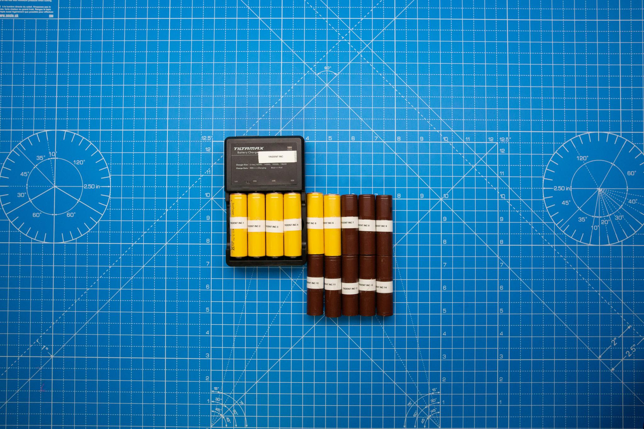 Top view of batteries on a blue grid design surface with a charger, showcasing organization and technology.